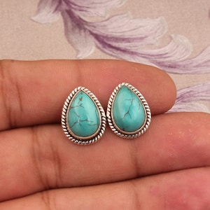 Op de afbeelding: Een paar zilveren druppelvormige oorbellen met turquoise stenen. De oorbellen hebben een touwachtig ontwerp rond de rand van de stenen.