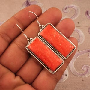 May include: A pair of silver dangle earrings with rectangular orange coral stones.