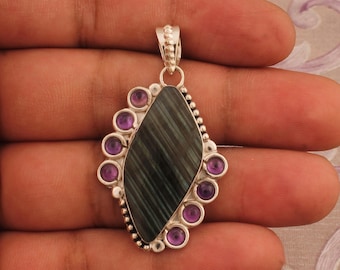 May include: Silver pendant with a dark green gemstone surrounded by a halo of small purple gemstones.