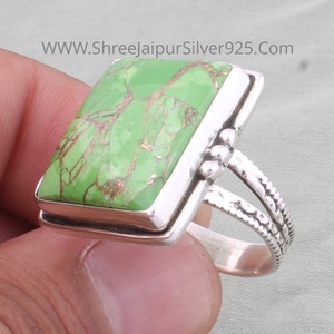 Könnte beinhalten: Ein Silberring mit einem grünen Türkis-Stein, der in einer quadratischen Fassung sitzt. Der Ring hat ein strukturiertes Band mit einem dekorativen Design.