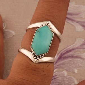 May include: A silver ring with a turquoise gemstone set in a geometric shape. The ring is designed with a V-shaped band and has a textured finish.