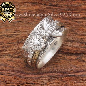 Könnte beinhalten: Ein silberner Drehring mit einem Bienen- und Blumendesign. Der Ring hat eine goldene Bander und ist mit der Nummer 925 graviert.