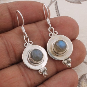 May include: Silver dangle earrings with a round, iridescent labradorite gemstone set in a silver bezel. The earrings have a simple, elegant design.
