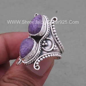 May include: A silver ring with two purple stones set in a decorative design. The ring has a beaded edge and a twisted band.