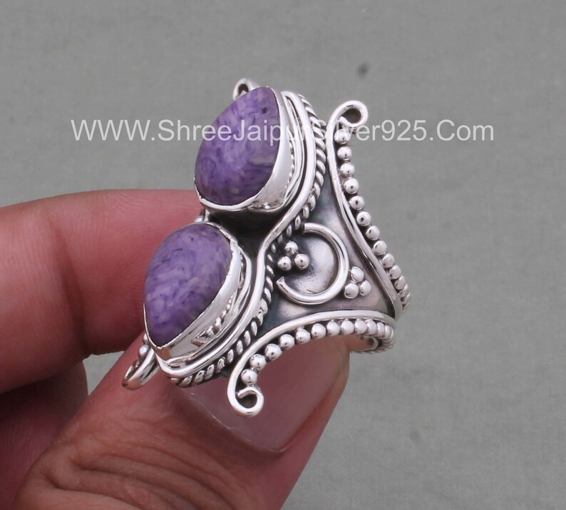 May include: A silver ring with two purple stones set in a decorative design. The ring has a beaded edge and a twisted band.