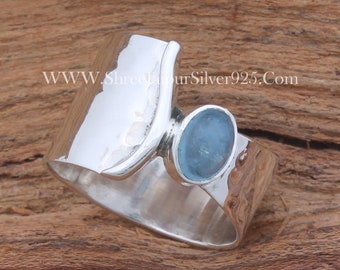 May include: A silver ring with a light blue gemstone set in a curved band. The ring has a hammered texture and is a unique and stylish piece of jewelry.