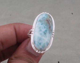 Op de afbeelding: Een zilveren ring met een grote ovale blauwe en witte edelsteen. De edelsteen heeft een draaiende structuur en is gezet in een zilveren zetting.