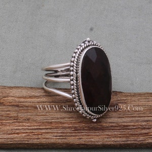 May include: A silver ring featuring a dark red oval gemstone set in a beaded bezel. The ring band has three bands.