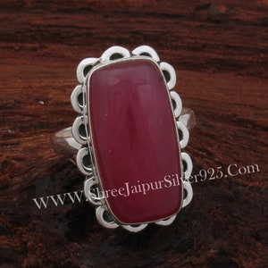May include: A silver ring with a large, rectangular, deep red stone. The stone is set within a decorative, scalloped frame. The website address www.ShreejaipurSilver925.com is visible on the ring.