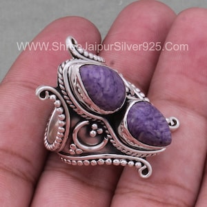 May include: A silver ring with two purple and white stones set in a decorative design. The ring has a wide band and intricate details.