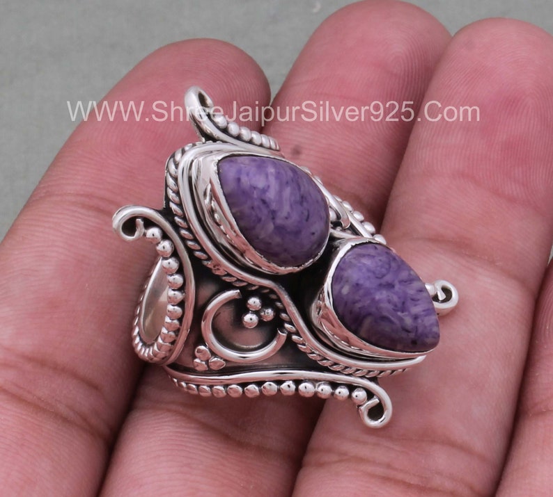 May include: A silver ring with two purple and white stones set in a decorative design. The ring has a wide band and intricate details.