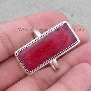Puede incluir: Un anillo de plata con una piedra preciosa rectangular roja. El anillo está engastado en una banda de plata con un acabado liso. La piedra preciosa es de color rojo intenso y tiene un ligero brillo. El anillo se muestra en un dedo.