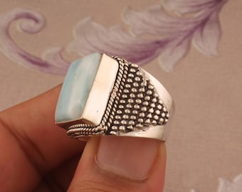 Puede incluir: Un anillo de plata con una piedra preciosa azul claro engastada en forma rectangular. El anillo tiene una banda texturizada con un diseño de cuerda.
