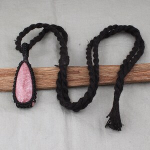 May include: A pink and white teardrop-shaped stone pendant on a black cord necklace. The necklace has a tassel at the end.