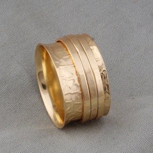 May include: Gold-toned spinning ring with a textured band. The ring is made of multiple bands that spin around each other.