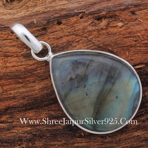 May include: A silver pendant with a teardrop-shaped labradorite gemstone. The gemstone has a blue-green iridescent sheen. The pendant is on a wooden surface.