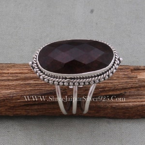 May include: A silver ring featuring a large, dark purple gemstone set in a bezel setting. The ring has an ornate band with a rope design and small beads.