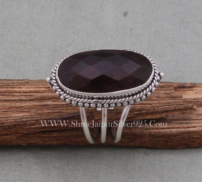 May include: A silver ring featuring a large, dark purple gemstone set in a bezel setting. The ring has an ornate band with a rope design and small beads.