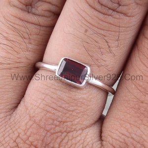 May include: A silver ring with a rectangular red gemstone. The ring is on a finger.