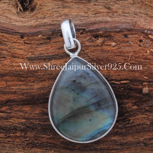 May include: A teardrop-shaped pendant with a silver setting and a blue and green labradorite gemstone. The pendant is on a wooden surface.