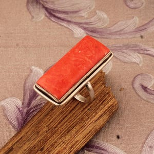 Puede incluir: Un anillo de plata con una piedra rectangular de coral naranja brillante.