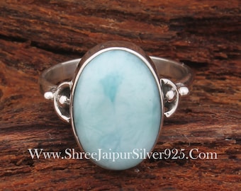 Puede incluir: Un anillo de plata con una piedra ovalada de color azul claro. El anillo tiene un diseño sencillo con pequeños detalles decorativos en los lados.