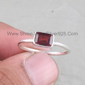 May include: A silver ring featuring a rectangular red gemstone. The ring has a plain band and the gemstone is set in a silver bezel.