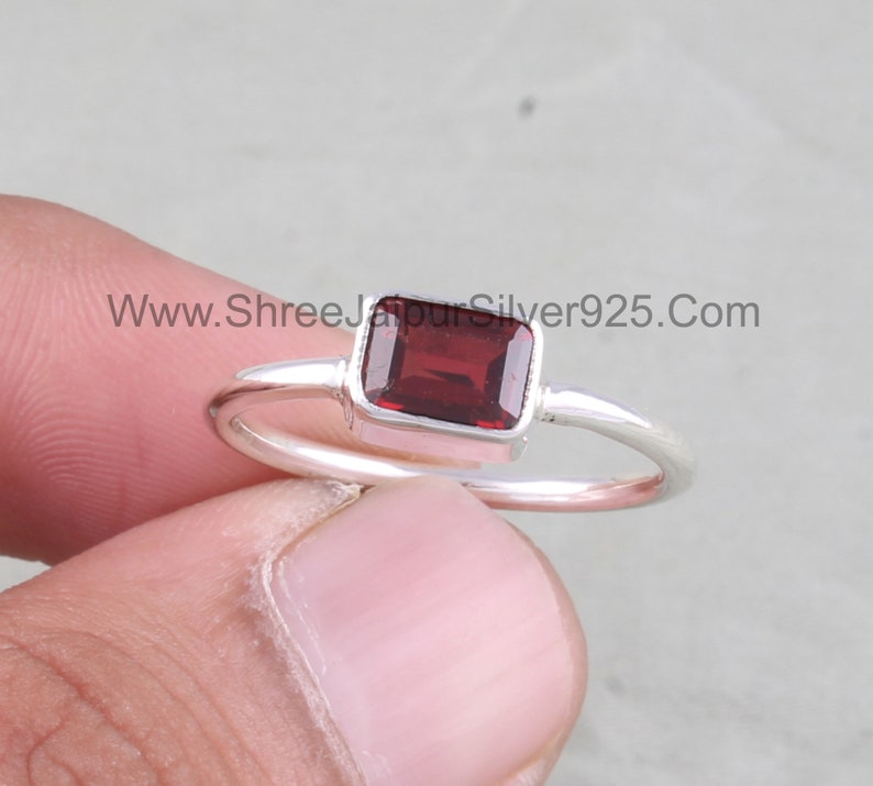 May include: A silver ring featuring a rectangular red gemstone. The ring has a plain band and the gemstone is set in a silver bezel.