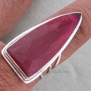 May include: A silver ring featuring a large, faceted, pink gemstone set in a pointed, geometric shape. The ring is worn on a finger.