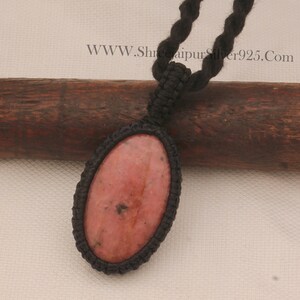 May include: A pink and black oval-shaped gemstone pendant on a black cord necklace. The pendant is set in a black cord macrame knot.