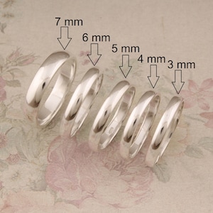 May include: Six silver rings of different widths, ranging from 3 mm to 7 mm, displayed on a floral patterned surface.