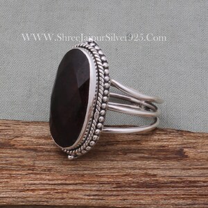 May include: A silver ring featuring a dark red gemstone set in a bezel setting. The ring has a triple band design and a beaded edge.
