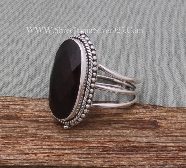 May include: A silver ring featuring a dark red gemstone set in a bezel setting. The ring has a triple band design and a beaded edge.