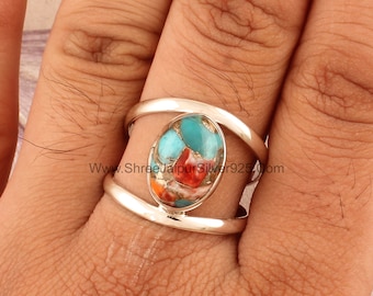 May include: A silver ring with a colorful oval-shaped stone set in the center. The stone is a mix of turquoise, red, and orange colors. The ring has a double band design.