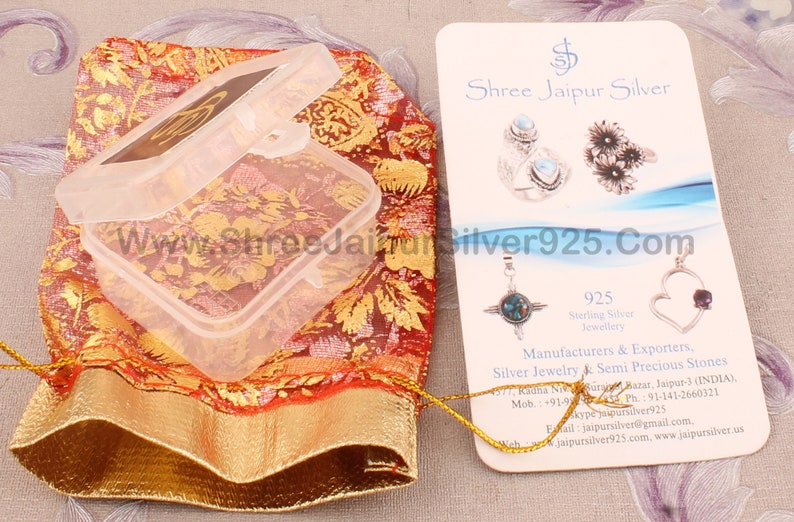 Pu&ograve; includere: Una scatola di gioielli in plastica trasparente aperta su un sacchetto a fantasia rosso e oro. &Egrave; visibile un biglietto da visita con immagini di gioielli e la scritta "Shree Jaipur Silver". Viene visualizzato anche l'indirizzo del sito web.