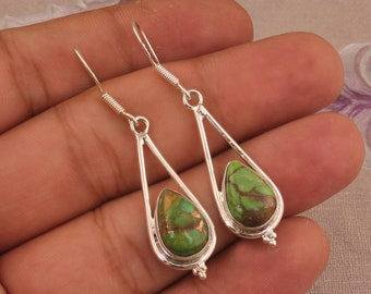 May include: A pair of silver dangle earrings featuring green turquoise stones. The stones are teardrop shaped and have a copper-like pattern.