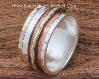 May include: A silver, copper, and brass spinning ring with a hammered texture. The ring is made of three bands that spin independently. The ring is on a wooden surface.