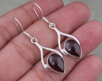 May include: A pair of silver dangle earrings with a teardrop-shaped garnet gemstone in each earring.