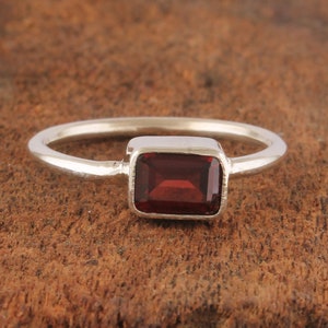 May include: A silver ring with a rectangular red gemstone.