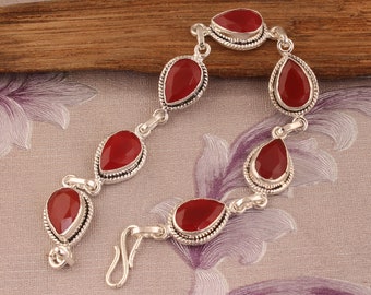 May include: A silver bracelet with six red gemstone teardrop-shaped charms. The bracelet has a hook clasp.