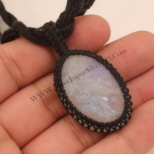 May include: A white moonstone pendant with a black macrame cord. The pendant is oval shaped and has a smooth, polished surface. The cord is tied in a knot at the top of the pendant.