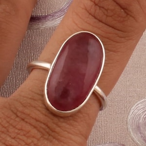 May include: A silver ring with a large, oval-shaped, deep pink gemstone.