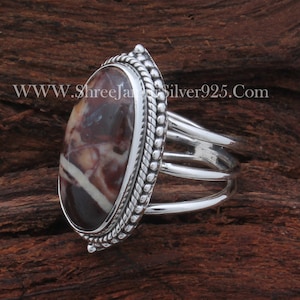 May include: A silver ring with a brown and white oval gemstone set in a rope-like border. The ring band has three silver bands.