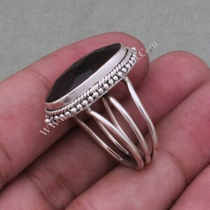 May include: A silver ring featuring a large, dark oval gemstone set in a beaded bezel. The ring band has three silver bands that wrap around the finger.