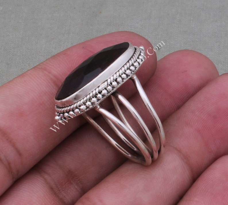 May include: A silver ring featuring a large, dark oval gemstone set in a beaded bezel. The ring band has three silver bands that wrap around the finger.
