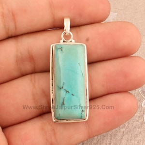 Könnte beinhalten: Ein Anhänger aus Silber mit einem Türkis-Edelstein. Der Anhänger ist rechteckig und hat eine hellblaue Farbe. Der Anhänger ist etwa 5 cm lang und 2,5 cm breit.