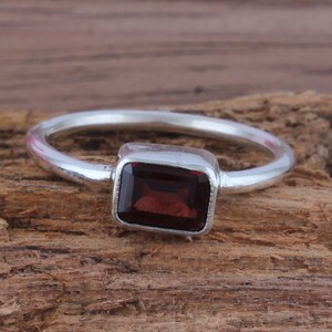 May include: A silver ring with a dark red rectangular gemstone.