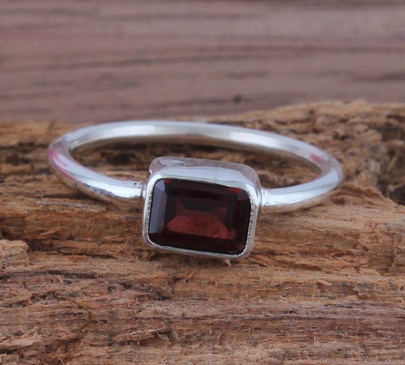 May include: A silver ring with a dark red rectangular gemstone.