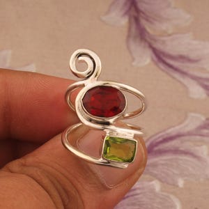 May include: A silver ring with a red and green gemstone setting. The ring has a unique, swirling design.