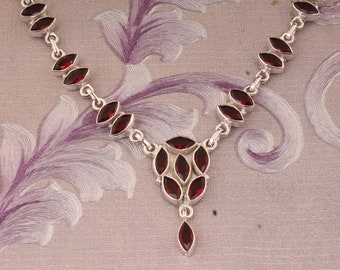 May include: A silver necklace with a pendant featuring a cluster of red gemstones. The necklace has a delicate chain and is adorned with small, red, marquise-shaped stones.